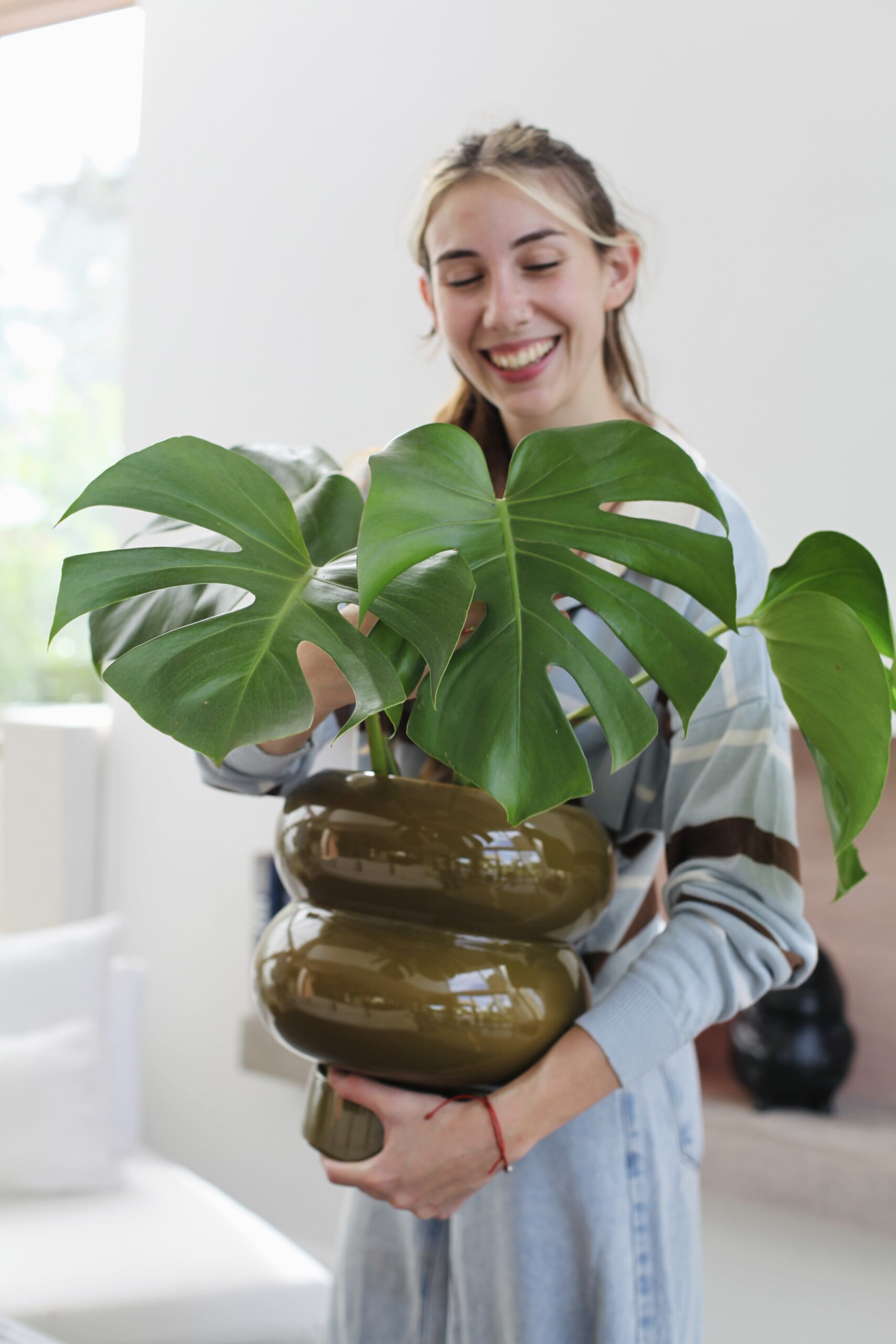 Mujer con Monstera deliciosa sana y frondosa en maceta cerámica verde oliva, cuidados riego y ubicación ideal